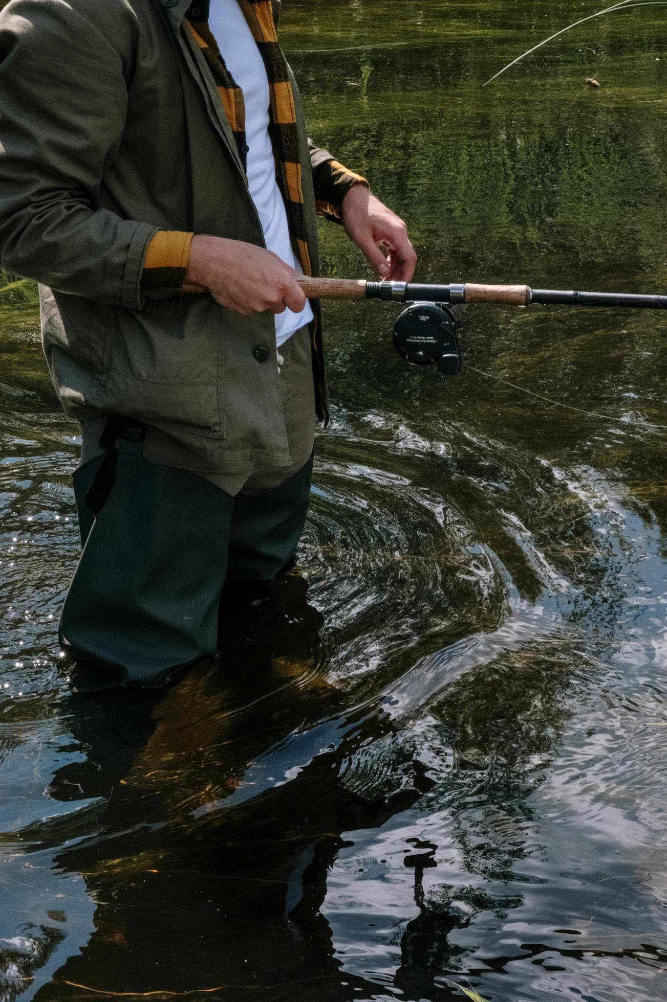 A man in waders fly fishing in a river during daytime.